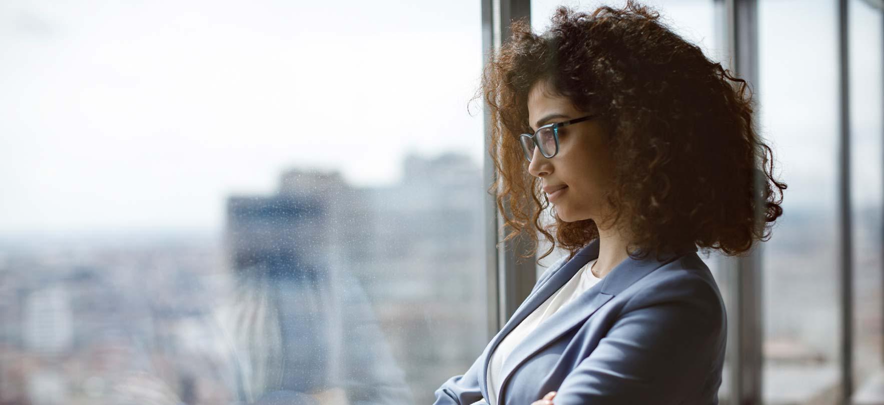Thoughtful businesswoman looking out the window over the city skyline from a high-rise office.