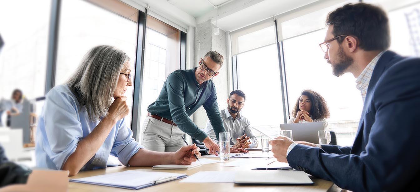 Business team engaged in a serious discussion around a meeting table in a bright, modern office.