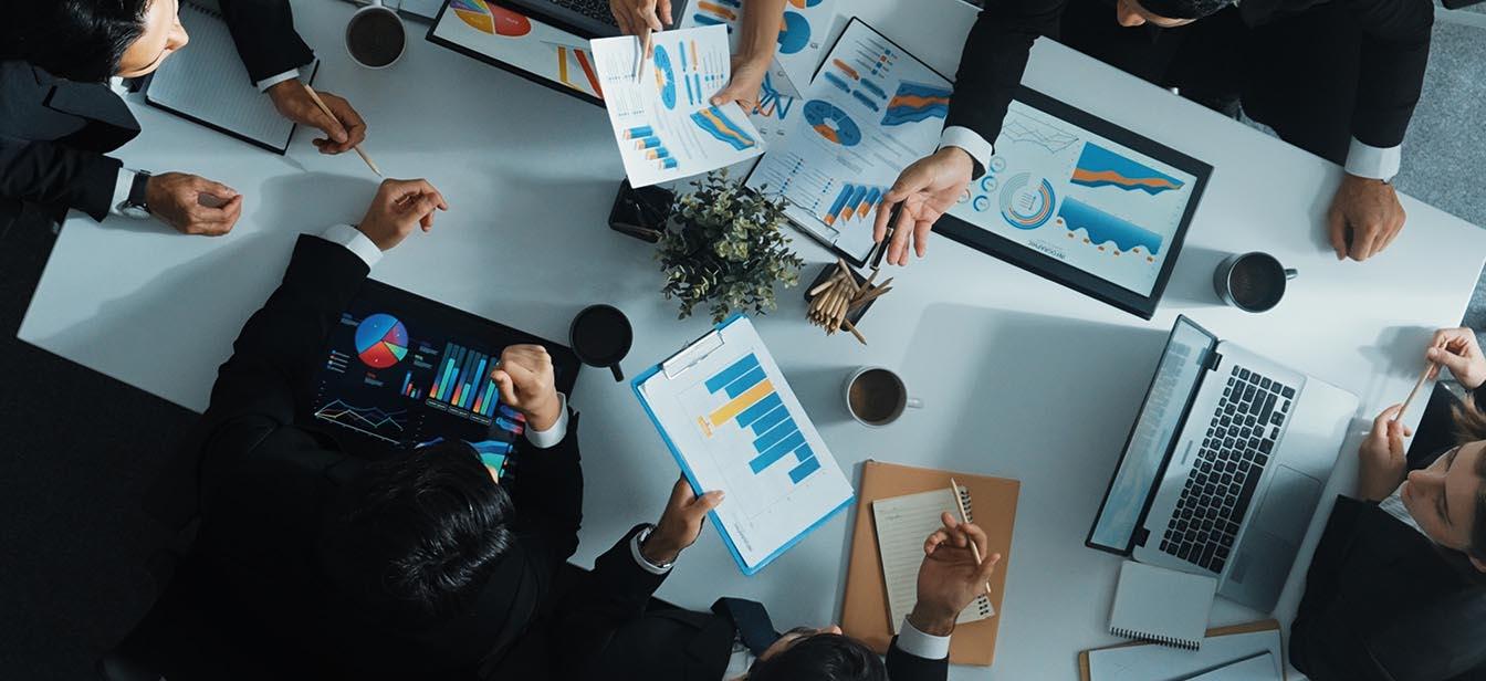 Top view of business professionals analyzing colorful charts and data during a meeting around a white table.