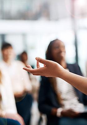 Hand gesturing during a discussion or presentation in a classroom with students in the background.