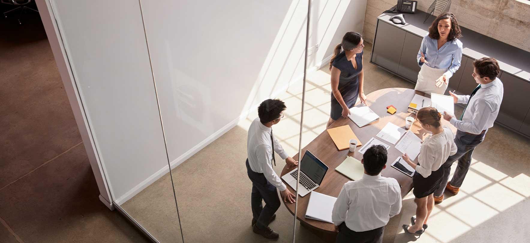 Team of professionals collaborating around a table in a bright, modern office meeting room viewed from above.