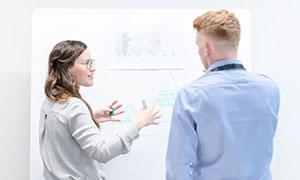 Two professionals discussing a diagram on a whiteboard in a bright, minimalist room.